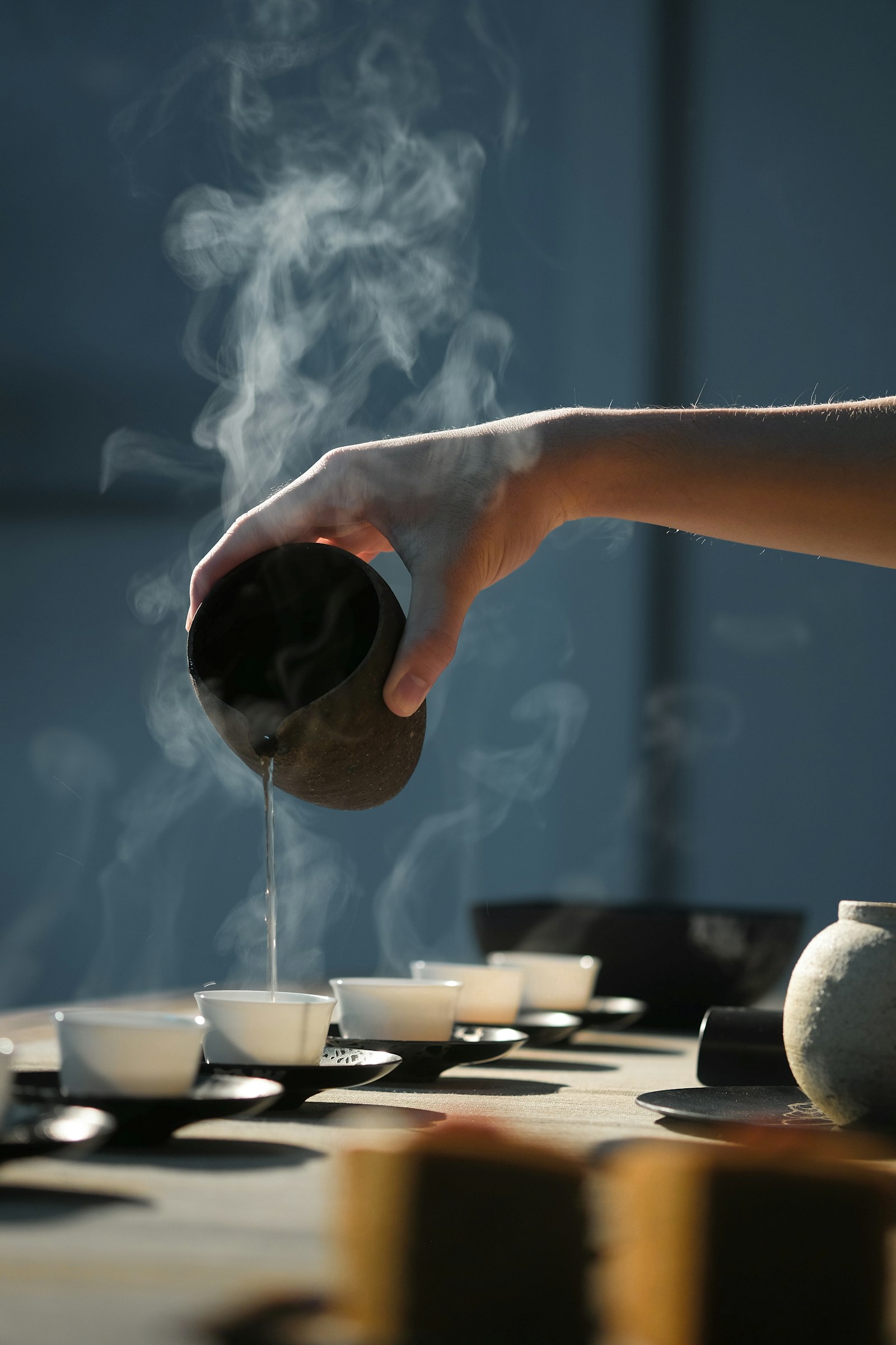 Tea poured from a small clay pot into a row of cups, with steam rising
